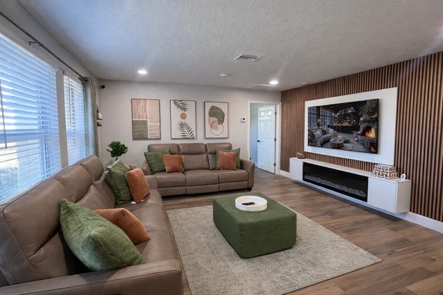 Living room at Serenity Living Home Care II on Holly Drive with two sofas, a green ottoman and a wall-mounted TV