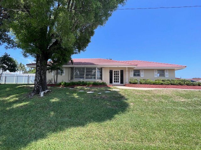 Front of a single-story Serenity Living home with a red roof, a lawn and a large shade tree